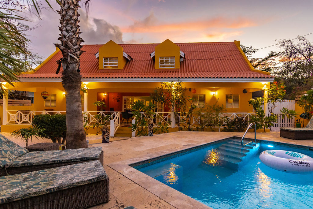 Loungers by the lit pool with the villa at dusk