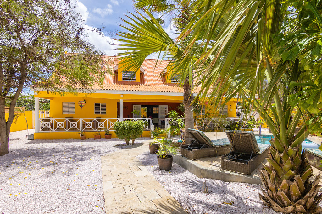 Sunny yellow facade with white veranda and pool loungers